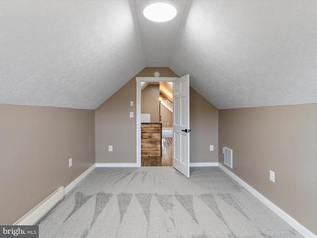 additional living space with a baseboard radiator, baseboards, a textured ceiling, and visible vents