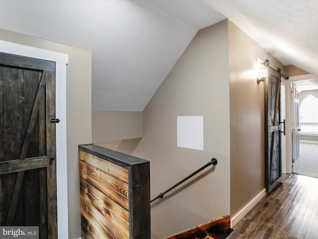 stairs with lofted ceiling, a barn door, wood finished floors, and a textured ceiling