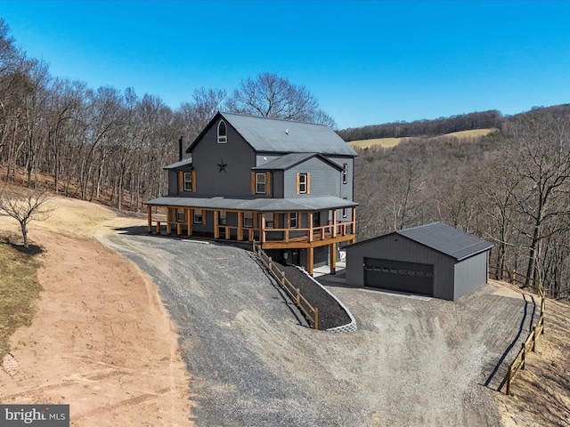 view of front facade featuring an outbuilding, driveway, a porch, a garage, and a view of trees