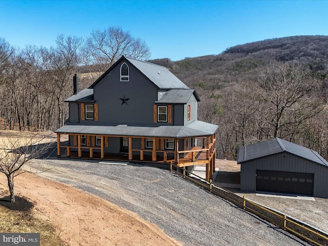 view of front of property featuring an outbuilding, fence, covered porch, a wooded view, and a garage