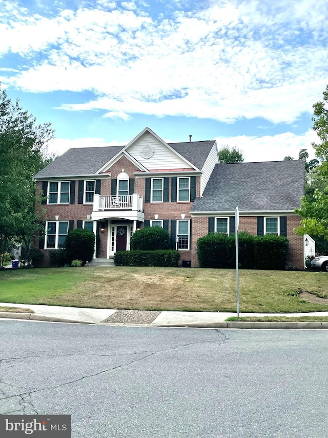 view of front of property featuring a front yard, a balcony, and brick siding