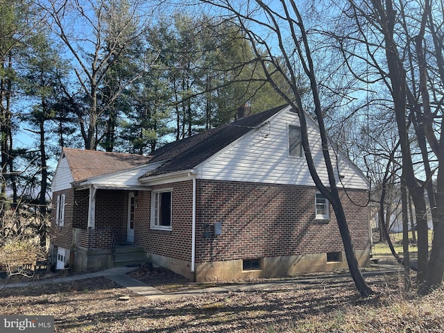 view of side of property with crawl space, brick siding, and a shingled roof