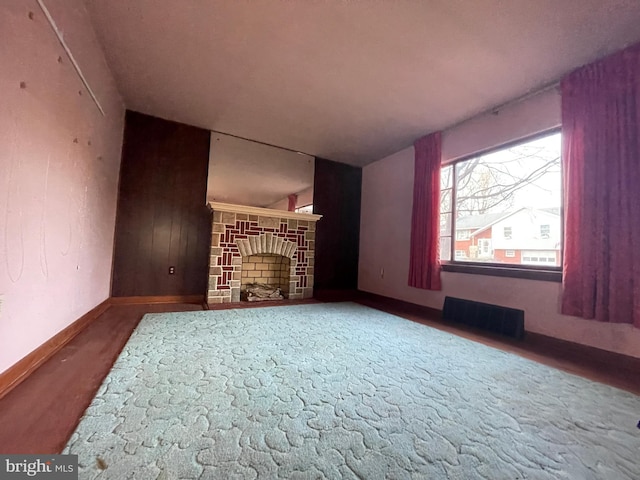 unfurnished living room with wood finished floors, a fireplace, visible vents, and baseboards