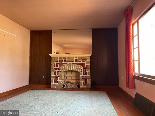 living room featuring wooden walls, wood finished floors, visible vents, baseboards, and a fireplace