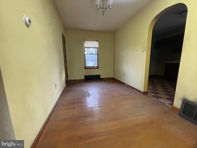 spare room featuring arched walkways, visible vents, baseboards, and wood finished floors