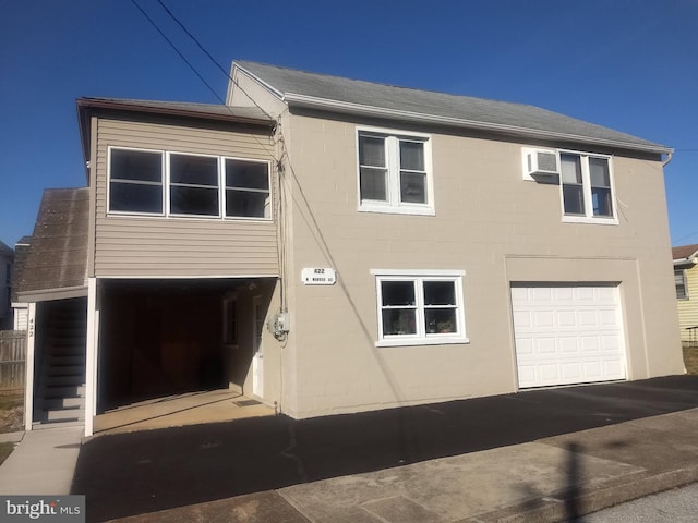 view of front facade with an attached garage, an AC wall unit, and roof with shingles