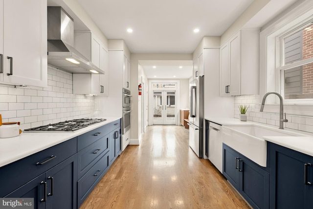 kitchen featuring blue cabinets, appliances with stainless steel finishes, wall chimney exhaust hood, and white cabinets