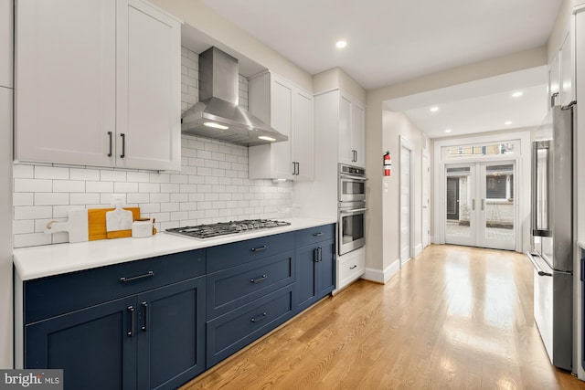 kitchen with blue cabinetry, light wood-style floors, appliances with stainless steel finishes, and wall chimney exhaust hood