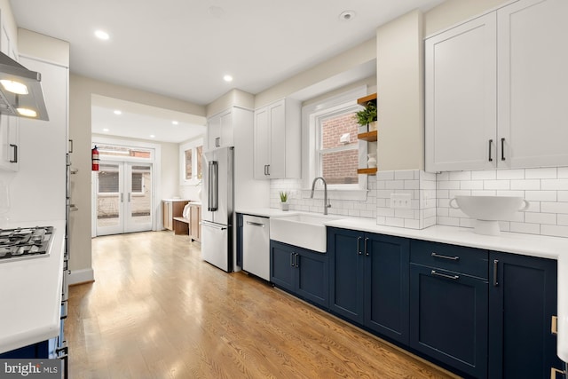 kitchen with light wood finished floors, blue cabinetry, a sink, appliances with stainless steel finishes, and white cabinetry