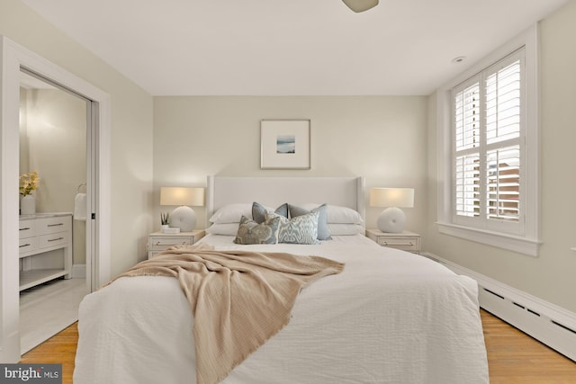 bedroom with a baseboard heating unit and light wood-style flooring