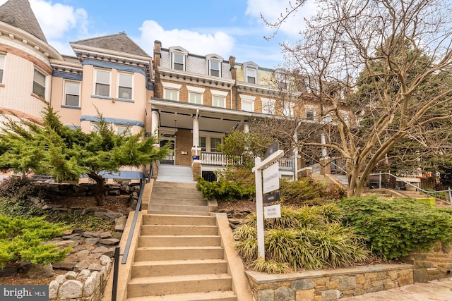 view of front of home featuring brick siding, stairway, mansard roof, and a high end roof