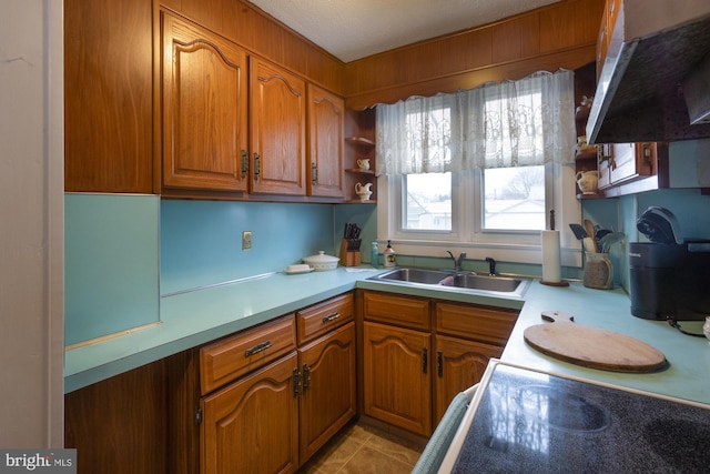 kitchen featuring a sink, brown cabinets, under cabinet range hood, and light countertops