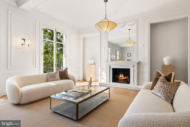 living room with wood finished floors, a lit fireplace, ornamental molding, and a decorative wall