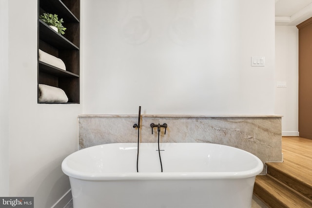 bathroom with a freestanding tub, wood finished floors, and baseboards