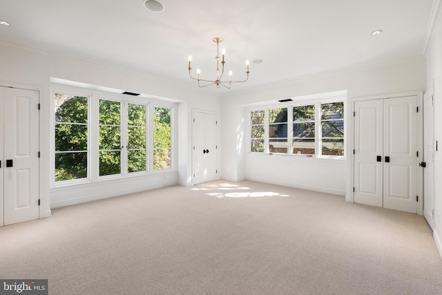 spare room featuring light carpet, a wealth of natural light, an inviting chandelier, and ornamental molding