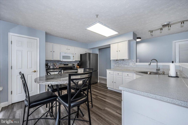 kitchen with decorative backsplash, appliances with stainless steel finishes, dark wood-style floors, white cabinets, and a sink