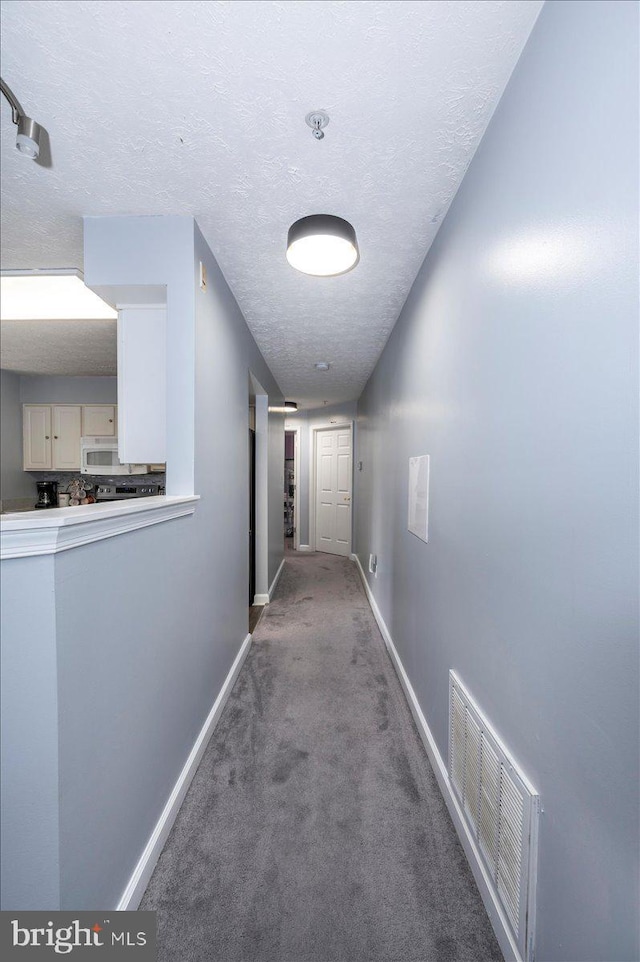 hall with visible vents, carpet flooring, a textured ceiling, and baseboards