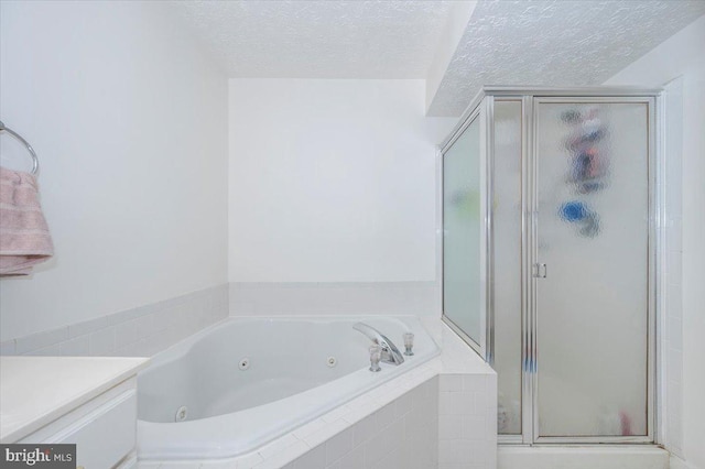 bathroom featuring a stall shower, a jetted tub, vanity, and a textured ceiling