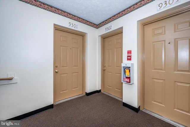 entrance foyer featuring baseboards, dark carpet, and a textured ceiling