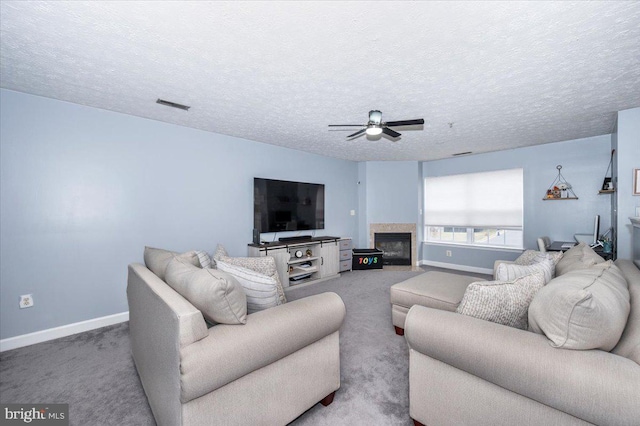 living area with visible vents, a ceiling fan, a textured ceiling, a glass covered fireplace, and carpet