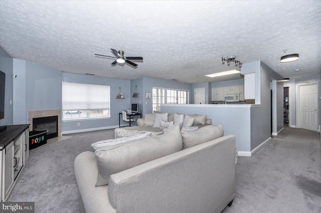 living area featuring a fireplace with flush hearth, a ceiling fan, baseboards, and light carpet