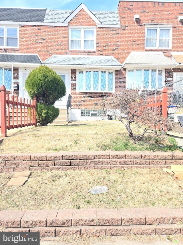 view of front of property with fence, a shingled roof, entry steps, a front lawn, and brick siding