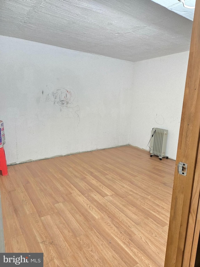 spare room with radiator heating unit and wood finished floors