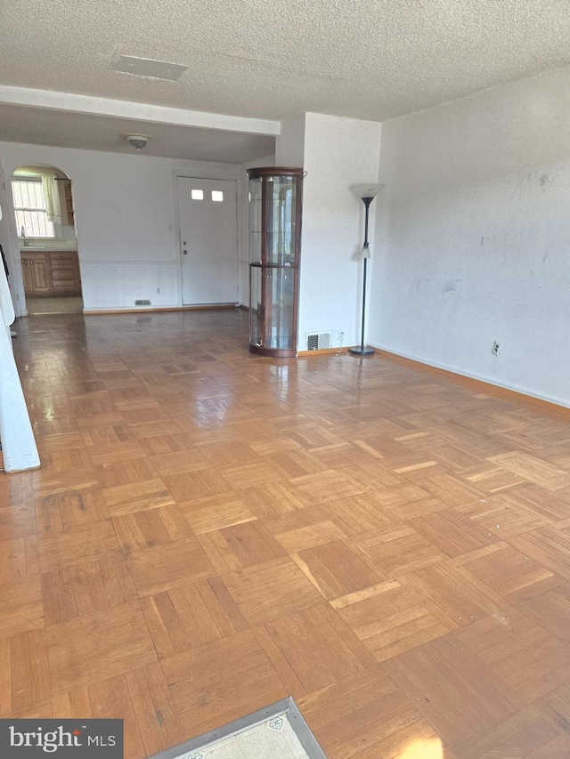 unfurnished room with baseboards, arched walkways, a textured ceiling, and visible vents