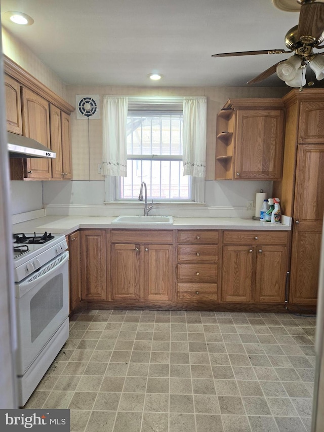 kitchen with brown cabinetry, gas range gas stove, a sink, light countertops, and under cabinet range hood