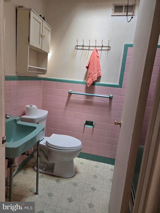 bathroom with a wainscoted wall, tile walls, toilet, and visible vents