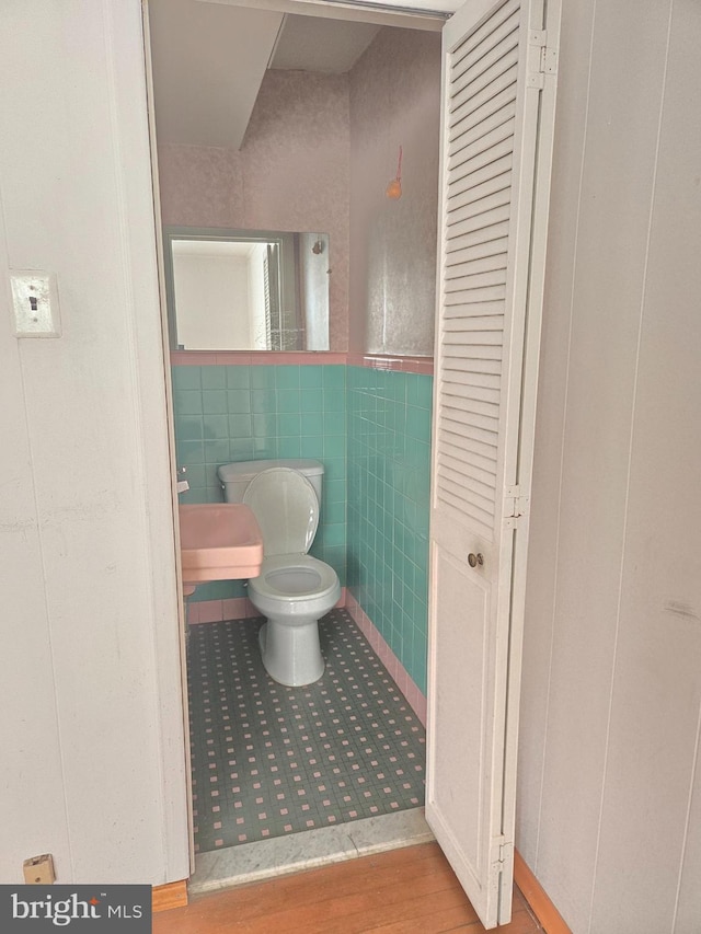 half bathroom with tile walls, toilet, wood finished floors, and wainscoting