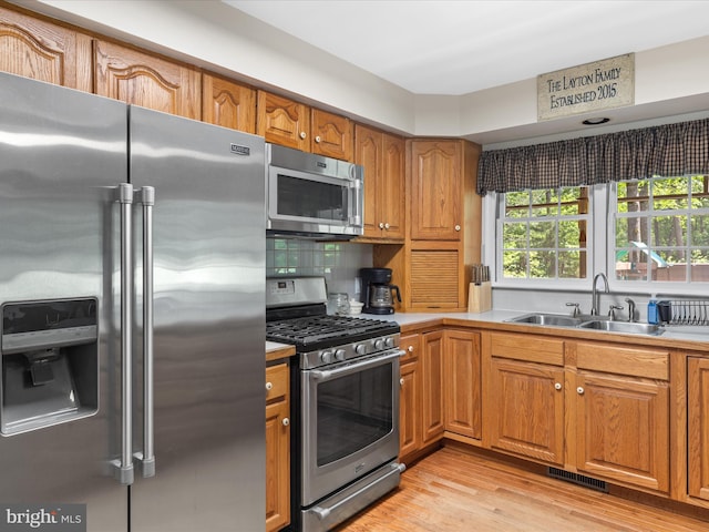 2446 Saint Lukes Rd, Salisbury, MD 21804 - kitchen with appliances with stainless steel finishes, a sink, light wood-style floors, brown cabinetry, and decorative backsplash