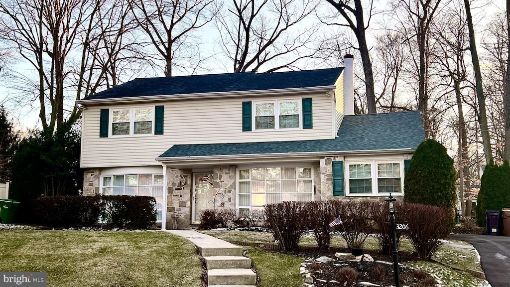 view of front facade featuring a front yard, stone siding, and roof with shingles