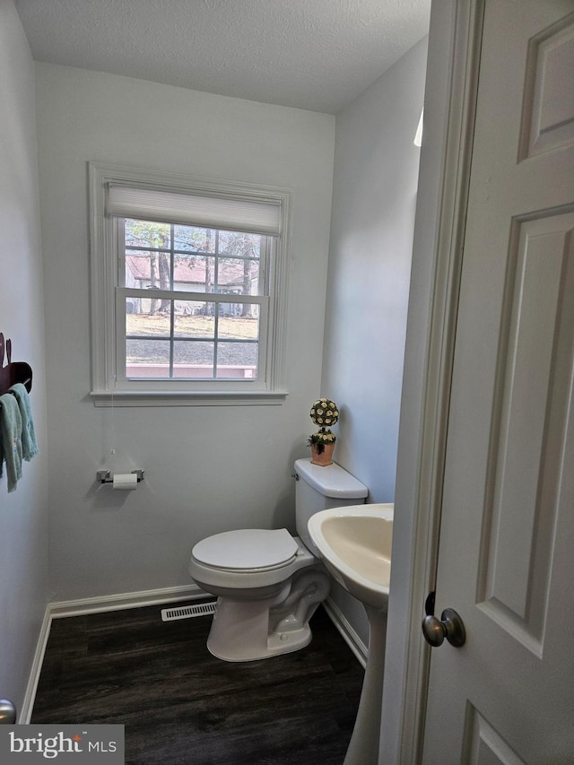 half bathroom featuring visible vents, a textured ceiling, toilet, and wood finished floors