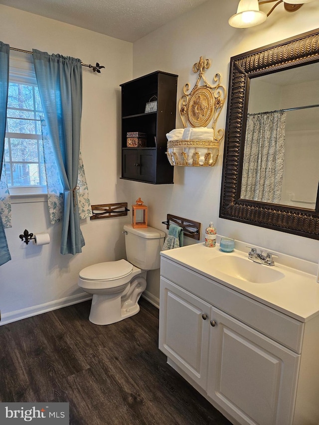 bathroom featuring toilet, a textured ceiling, wood finished floors, baseboards, and vanity