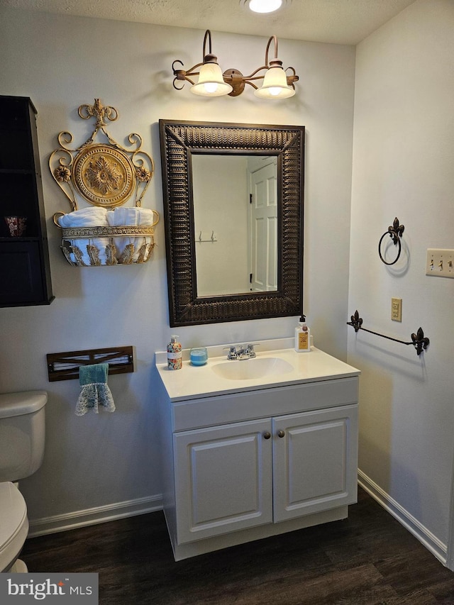 bathroom featuring toilet, vanity, baseboards, and wood finished floors