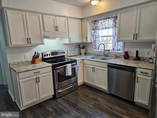 kitchen featuring dark wood finished floors, a sink, white cabinets, under cabinet range hood, and appliances with stainless steel finishes