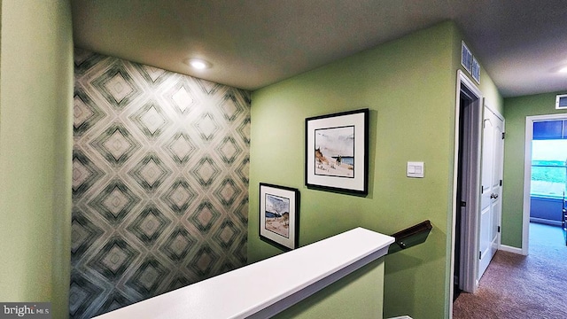 corridor featuring an upstairs landing, baseboards, visible vents, and dark colored carpet