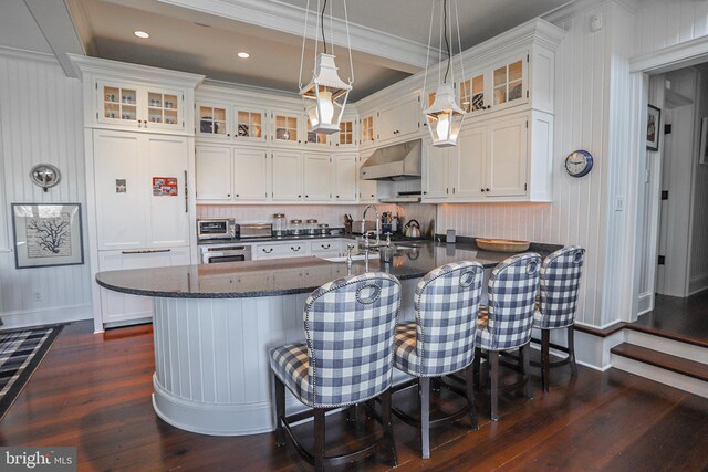 1 103rd St, Stone Harbor, NJ 08247 - kitchen with dark wood-type flooring, under cabinet range hood, a peninsula, a kitchen breakfast bar, and white cabinetry