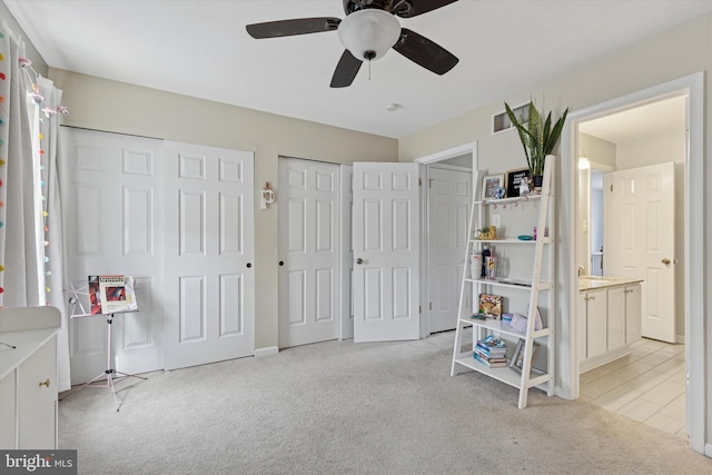 unfurnished bedroom featuring two closets, light colored carpet, and a ceiling fan