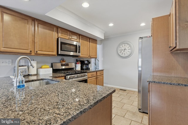 kitchen featuring ornamental molding, a sink, dark stone counters, appliances with stainless steel finishes, and baseboards