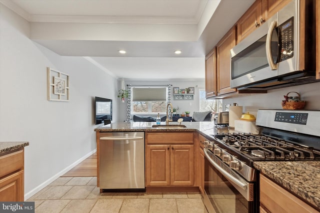 kitchen featuring ornamental molding, stone counters, a peninsula, stainless steel appliances, and a sink