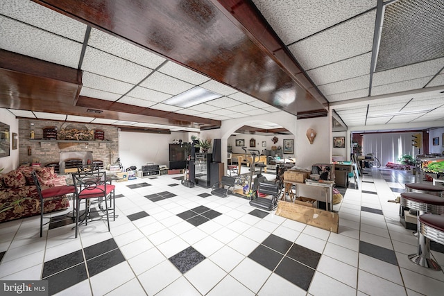 misc room with arched walkways, a drop ceiling, and tile patterned floors