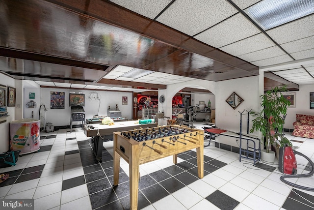 recreation room featuring arched walkways, baseboards, a paneled ceiling, and tile patterned flooring