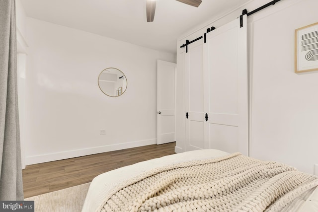 bedroom featuring baseboards, a ceiling fan, a barn door, and wood finished floors