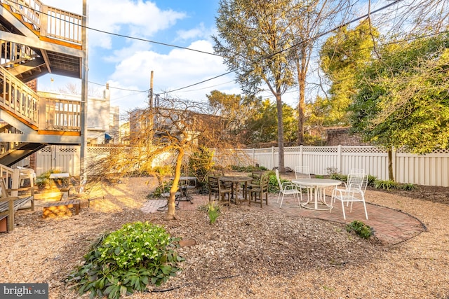 view of yard with a patio area, outdoor dining area, stairs, and a fenced backyard