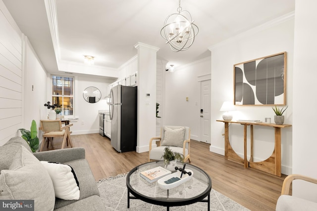 living room with light wood-style flooring, a notable chandelier, baseboards, and ornamental molding