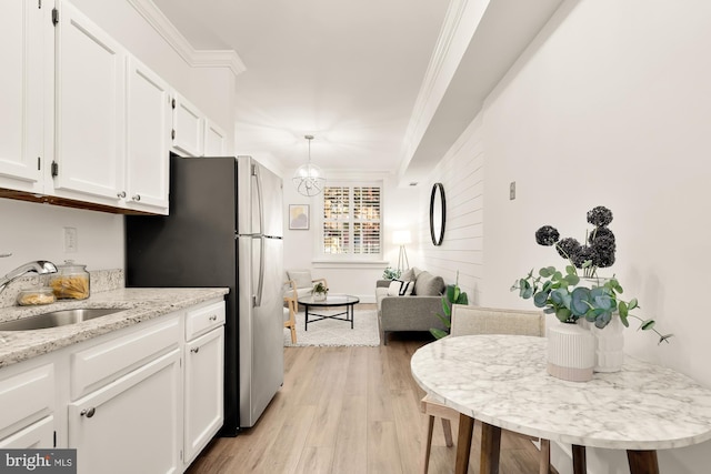 kitchen with a sink, light wood finished floors, crown molding, and white cabinetry