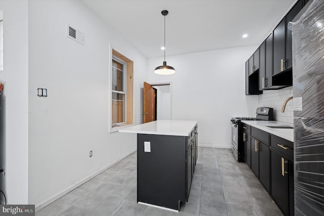 kitchen with dark cabinetry, stainless steel gas range, light countertops, tasteful backsplash, and a center island