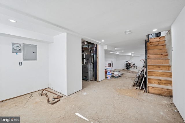 finished basement featuring stairs, electric panel, visible vents, and heating unit